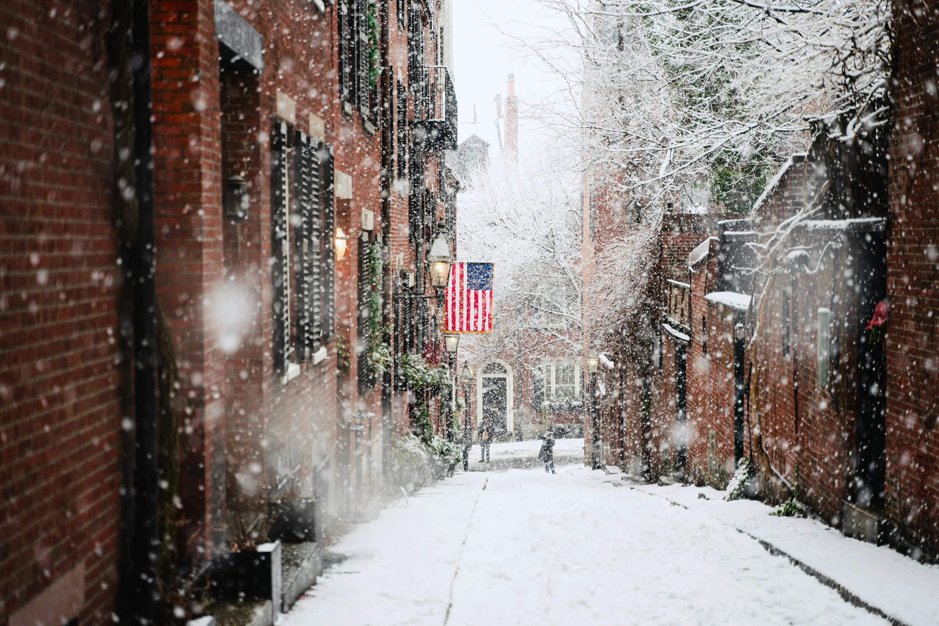 A snow-covered alley in Beacon Hill with an American flag hanging from a brick townhouse