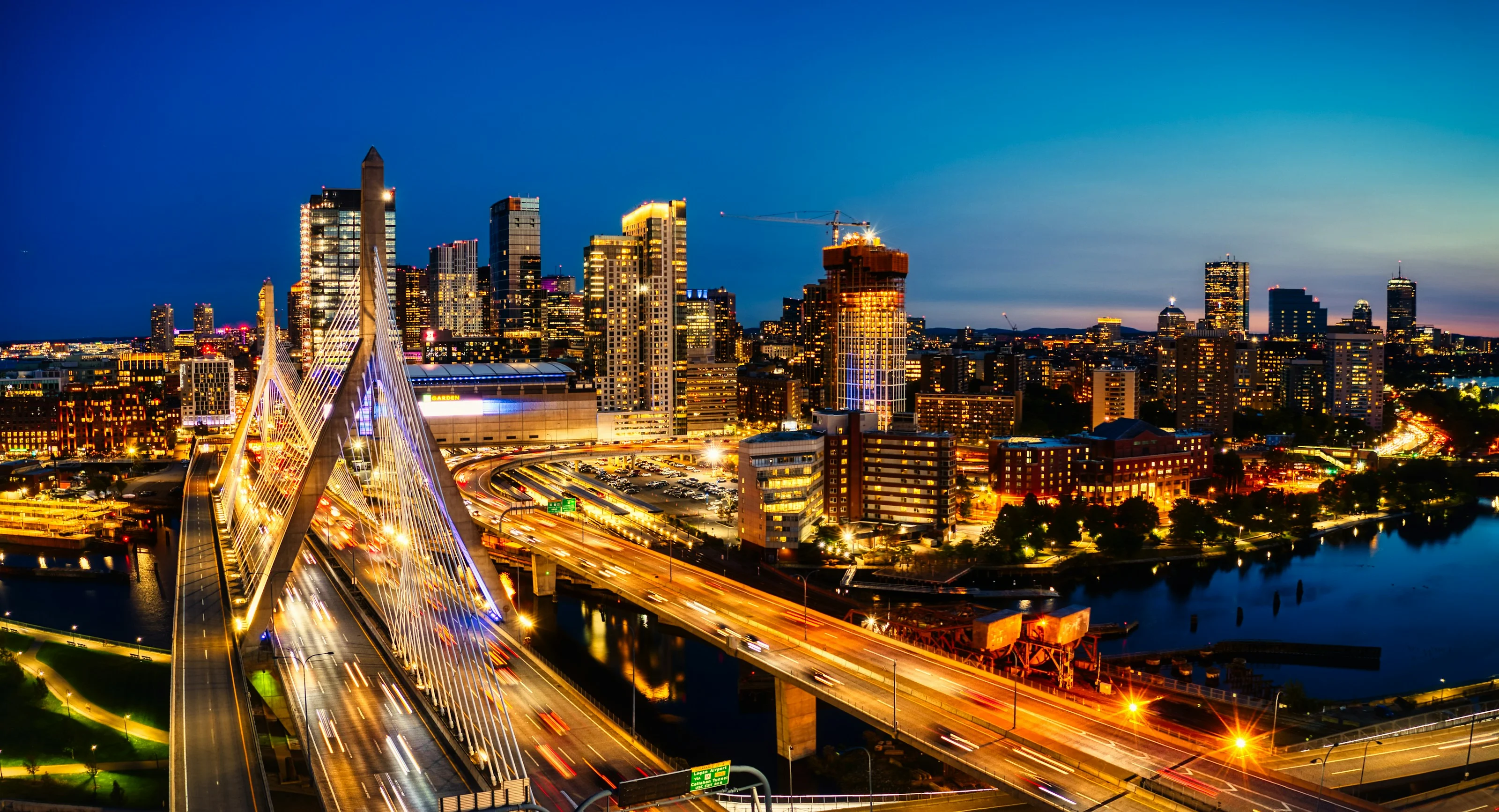 Boston's skyline at night with the illuminated Zakim Bridge in the foreground